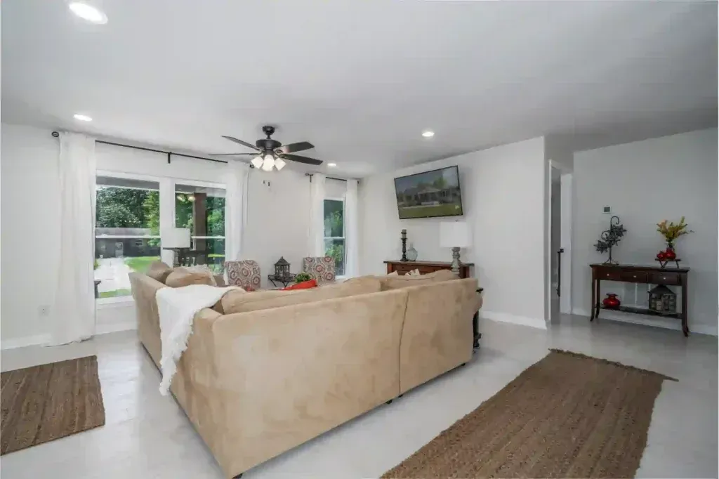 Spacious living room with tan sectional sofa, TV, and large windows with sheer curtains.