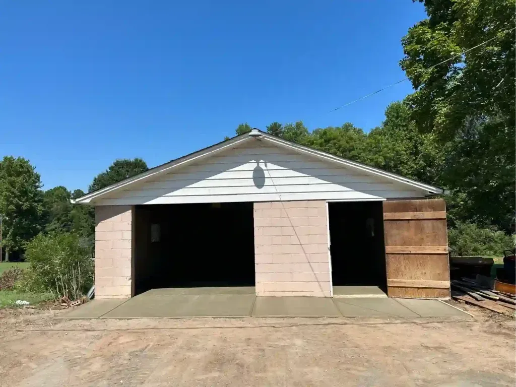Garage with open doors, freshly poured concrete, blue sky.