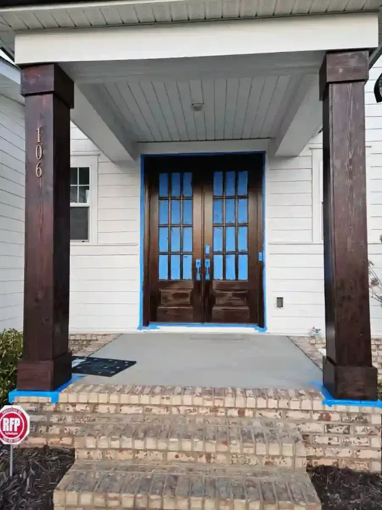 Front porch with stained brown columns, double brown doors, white siding, and brick steps.