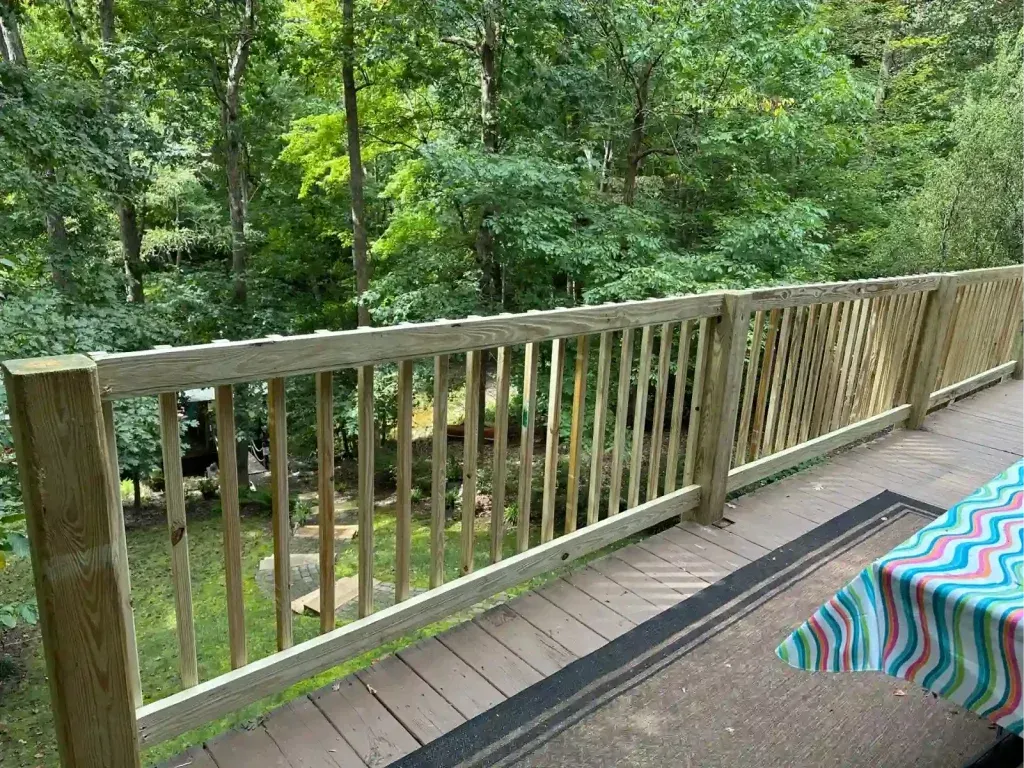 Deck railing with lattice panels, surrounded by trees. Part of a table with a patterned tablecloth is visible.
