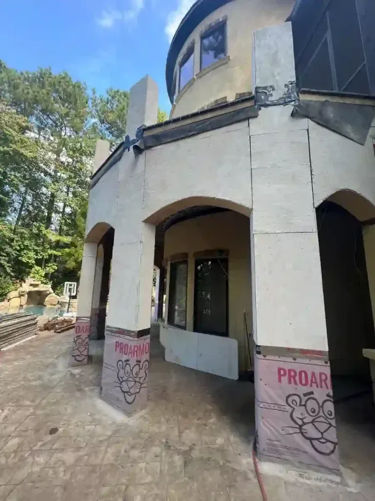 Exterior of a building with arches and columns, unfinished construction evident, pink insulation visible.