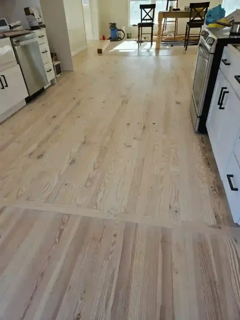 Light wood floor in a kitchen with white cabinets, stainless steel appliances, and a table with chairs in the background.