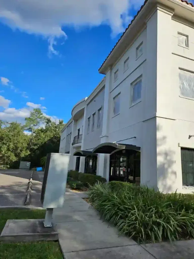 White two-story building with dark awnings and a walkway. Blue sky overhead.