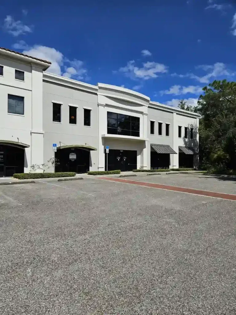 Gray and white commercial building with a blue sky and parking lot.