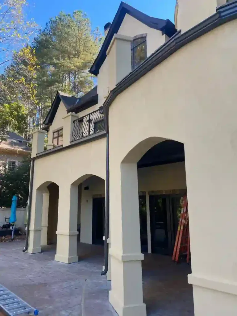 Beige stucco building with arched openings and black trim; trees in the background.