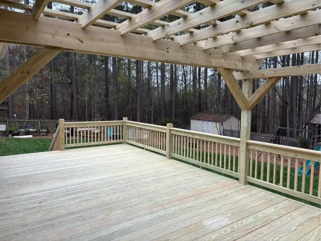 Wooden deck with pergola, railing, and view of trees.