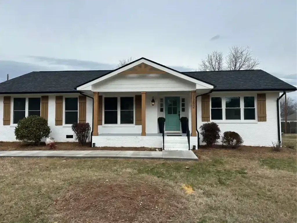 White brick ranch house with black roof, teal door, brown shutters.