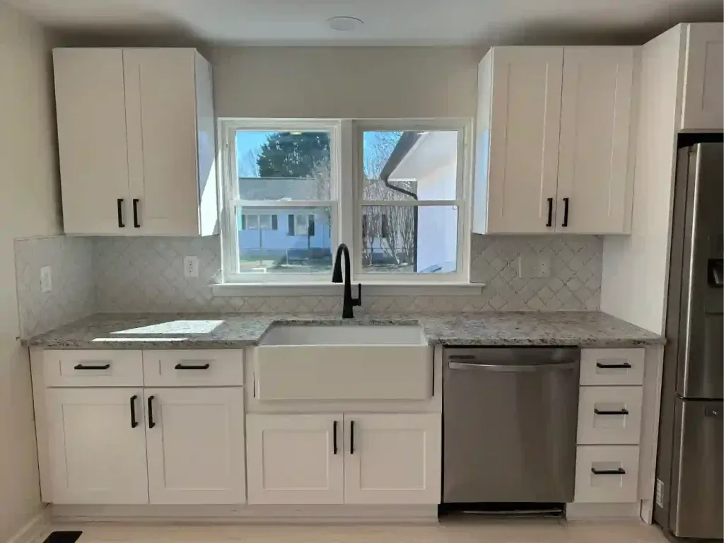 White kitchen with granite countertops, farmhouse sink, black faucet, and stainless steel appliances.