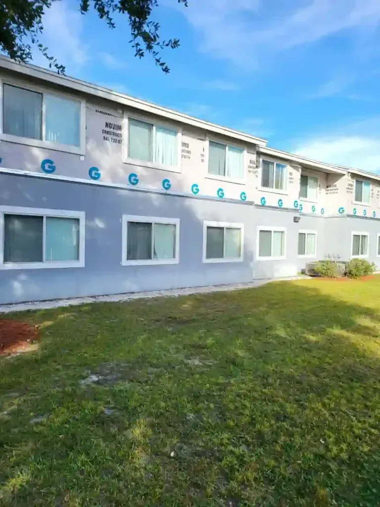 Apartment building with light blue and white facade, windows, and green grass lawn.