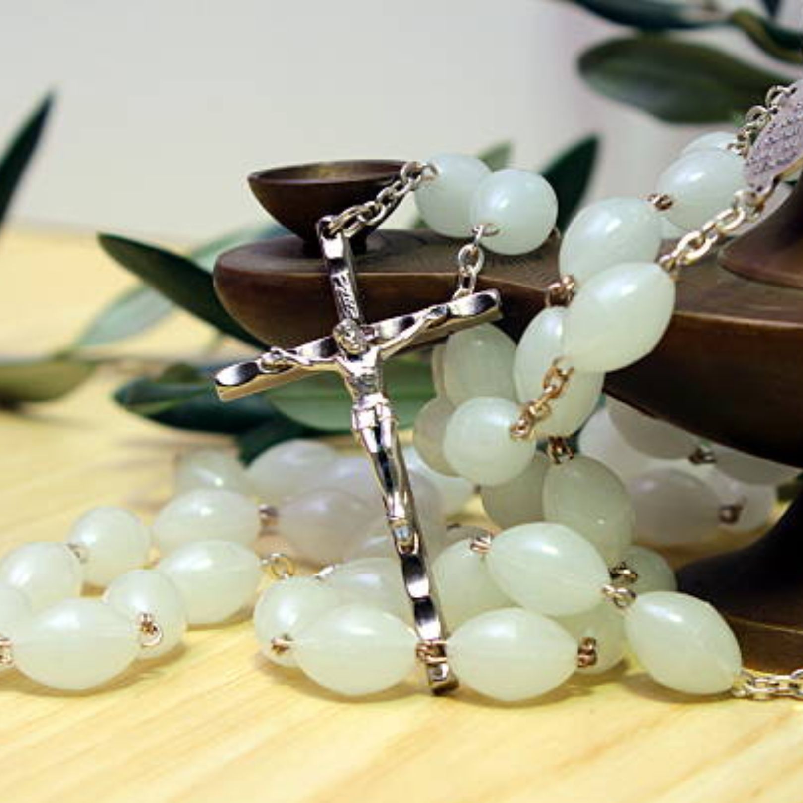 Silver crucifix necklace with pale jade beads on a wooden surface