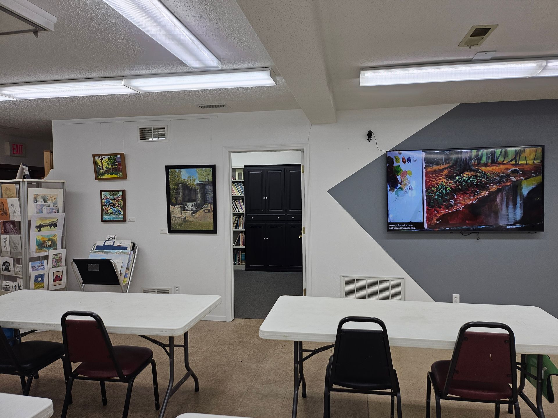 A room with tables and chairs and a flat screen tv on the wall.
