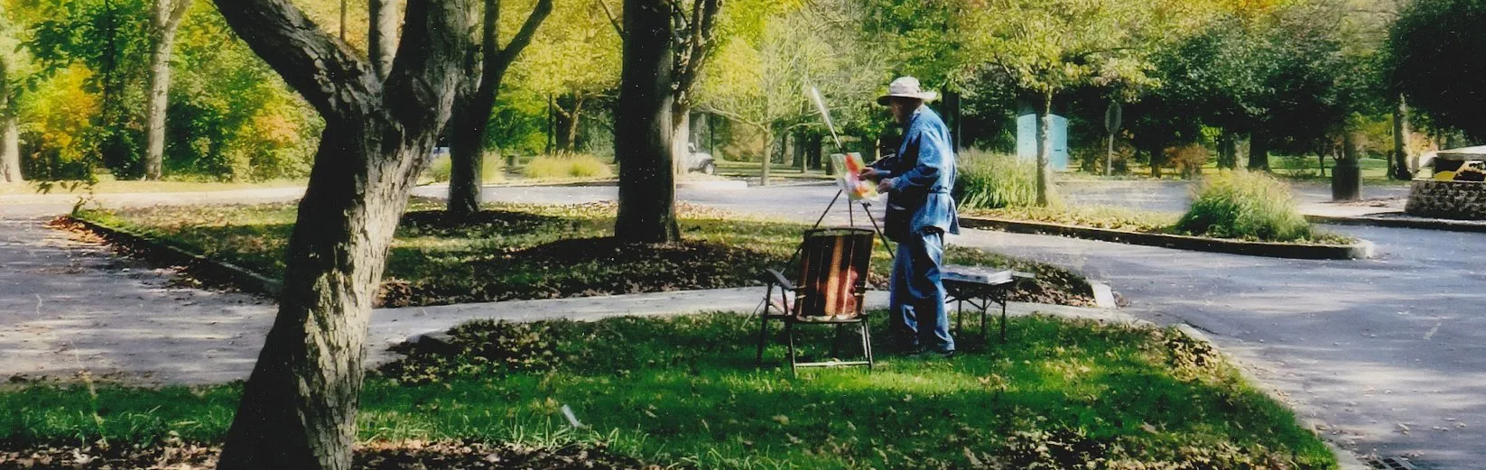A man is standing in the grass painting a picture.