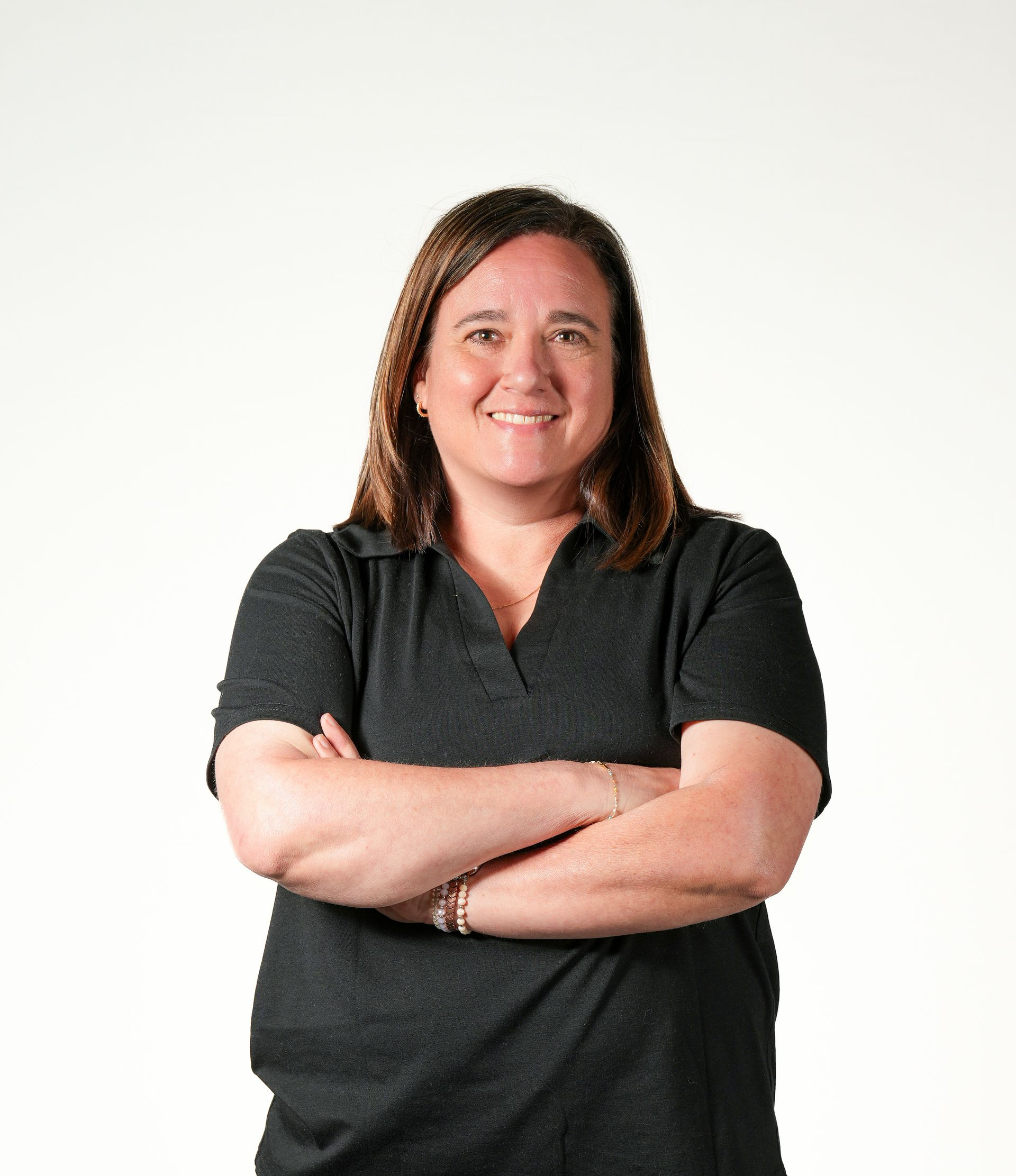 A woman in a grey shirt is standing with her arms crossed and smiling.