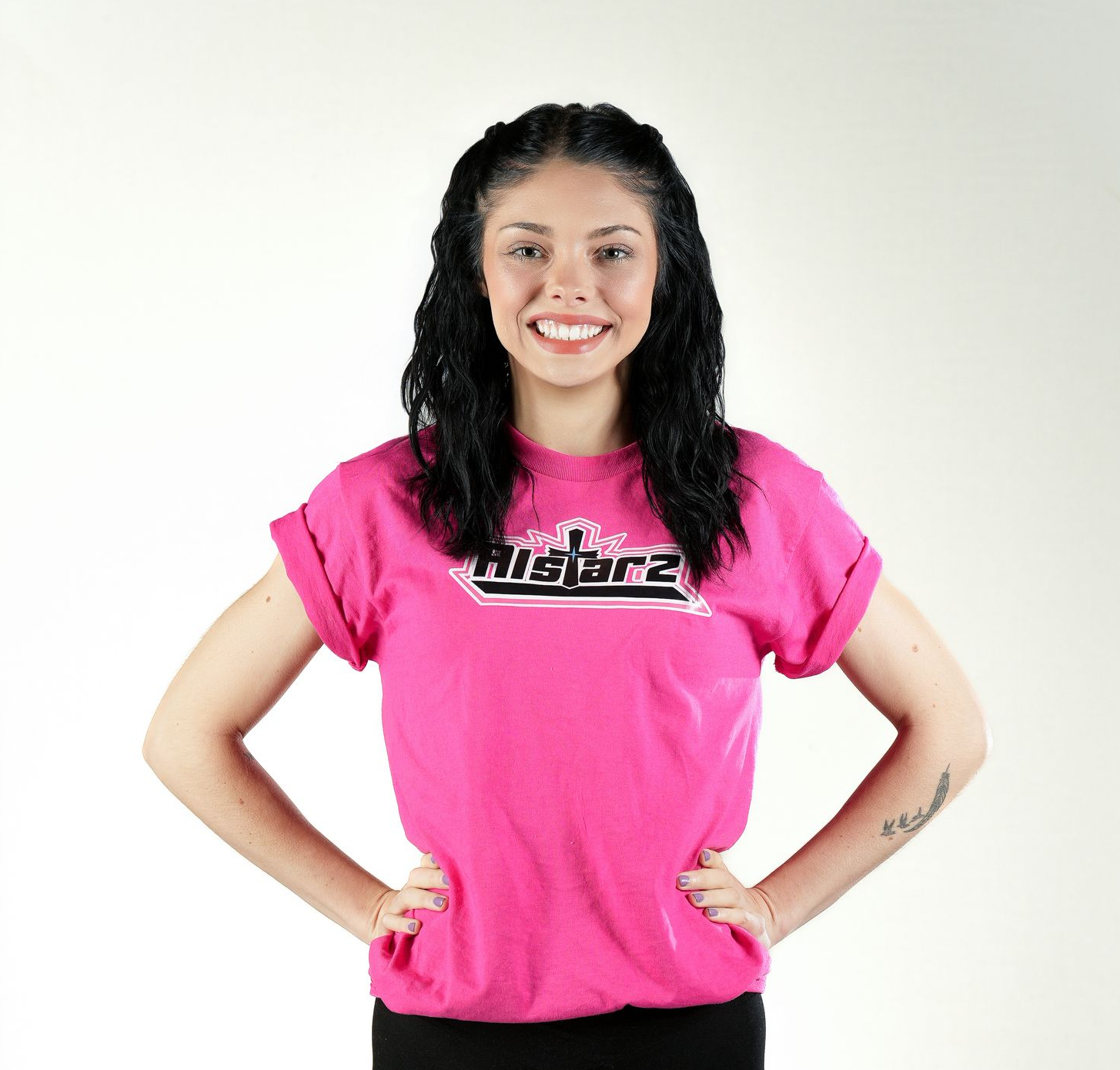 A woman wearing a blue aca t-shirt is standing with her hands on her hips.