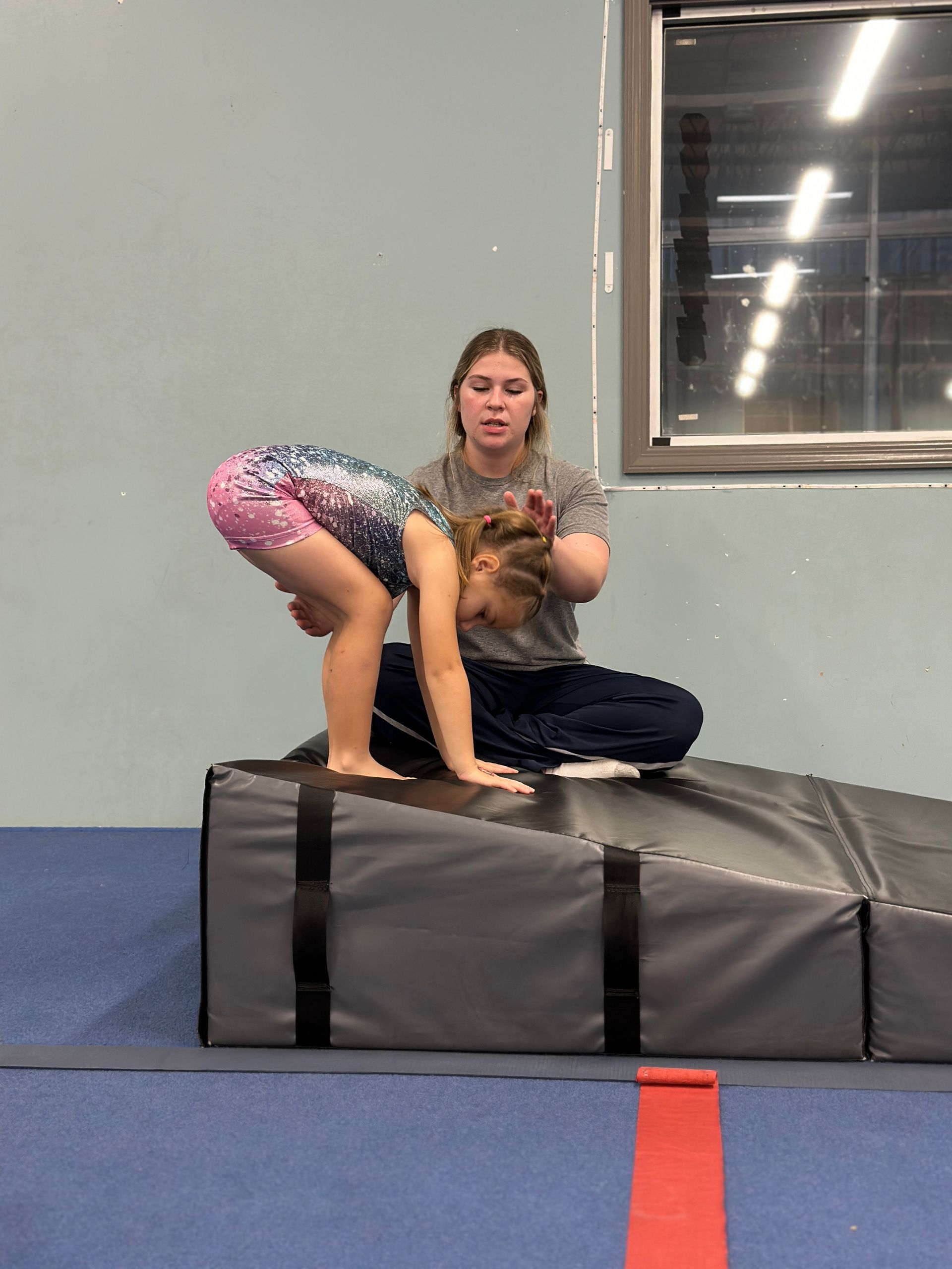 A woman is helping a young girl do a handstand on a mat.