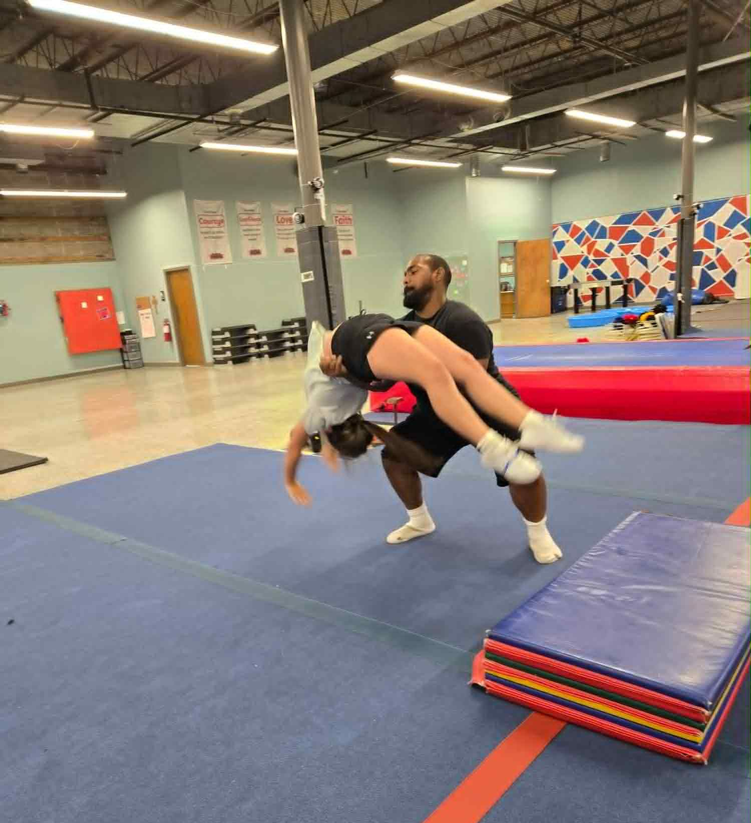 A girl is laying on a purple and yellow rocker in a gym