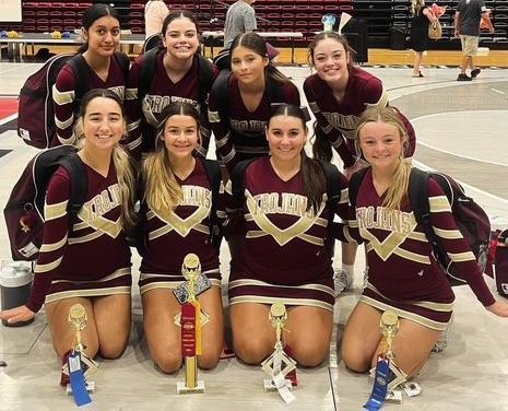 A group of cheerleaders are posing for a picture with trophies.