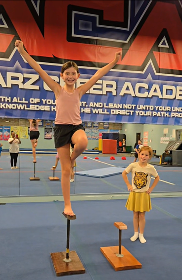 A woman is helping a little girl stretch on a yoga mat.