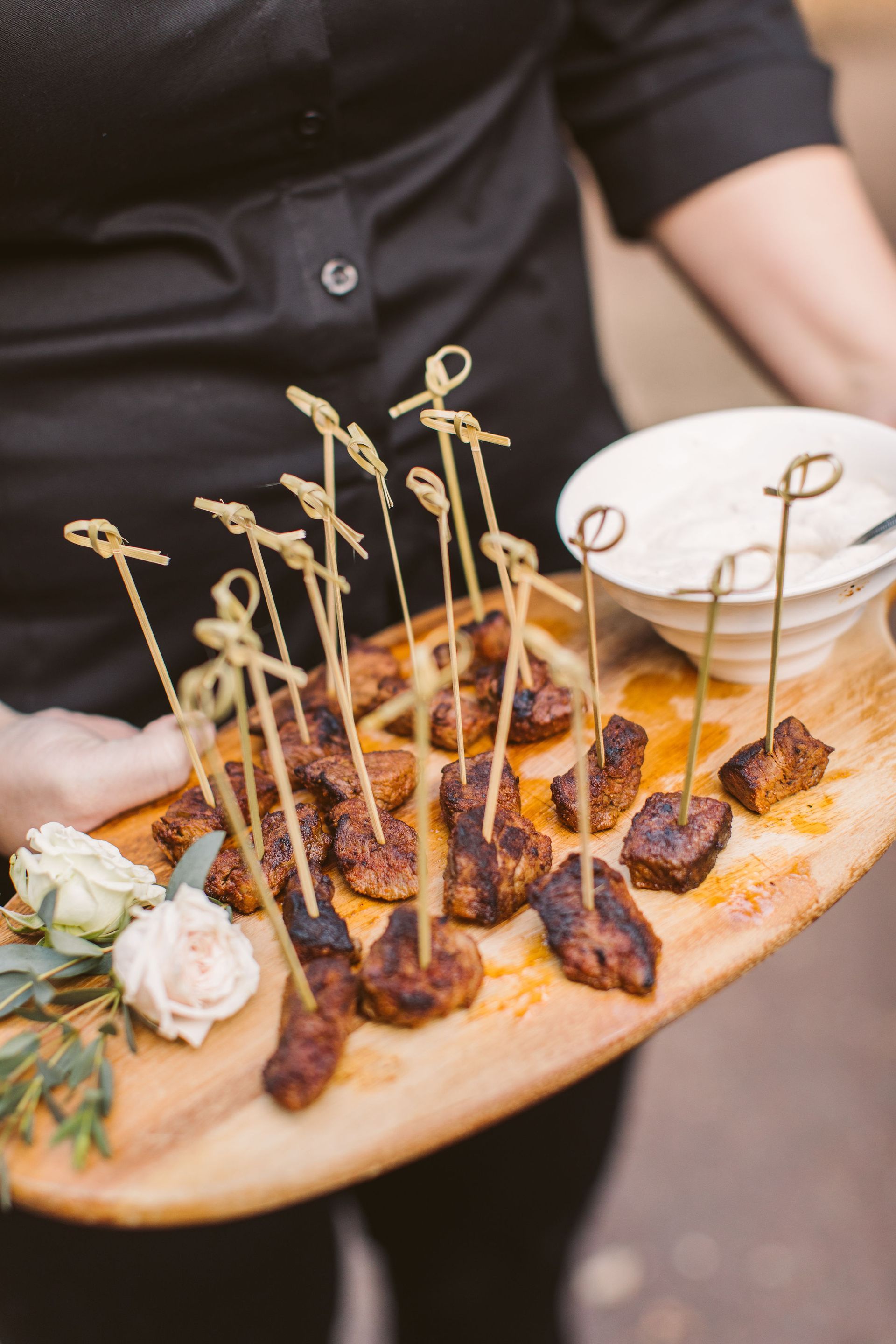 A person is holding a wooden tray of food on toothpicks.