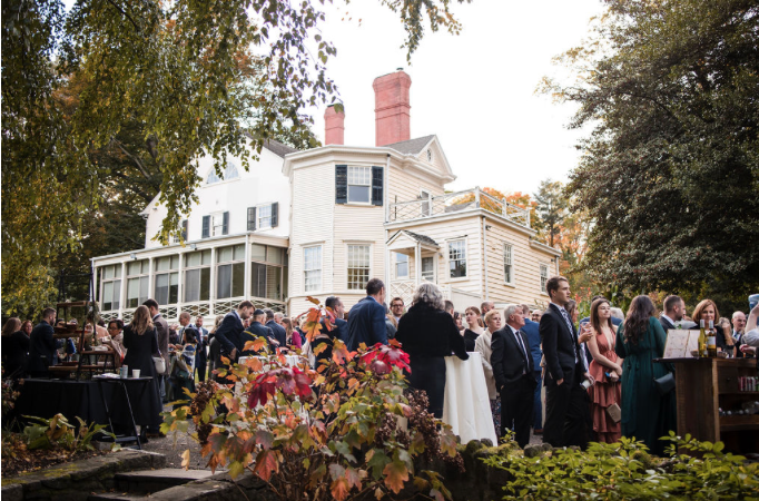 A group of people are standing in front of a large white house.