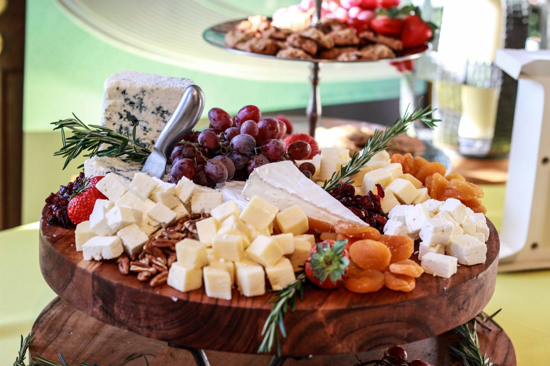 A wooden cutting board filled with cheese , grapes , nuts and dried fruit.