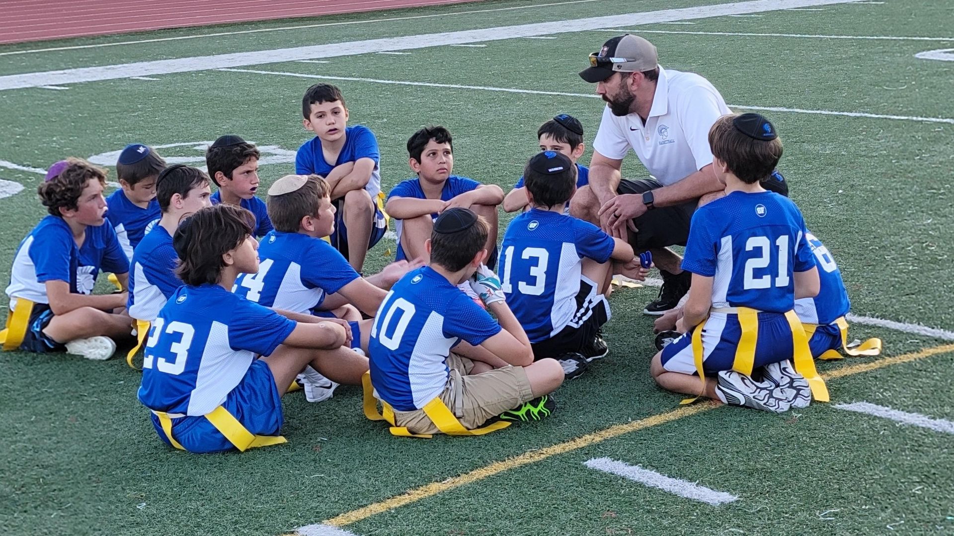 A group of young boys are sitting in a circle on a football field while a coach talks to them