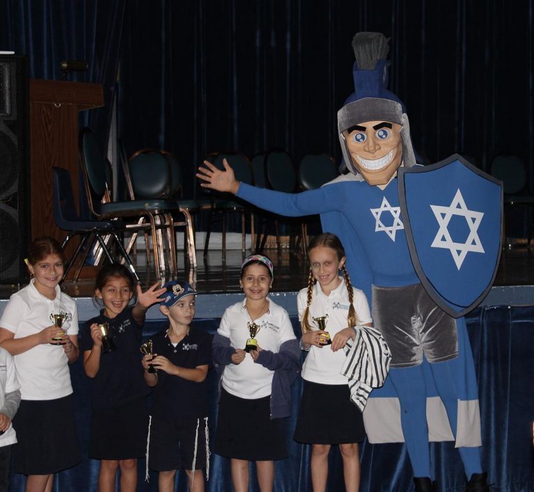 A group of children standing next to a mascot with a blue shield with a star on it