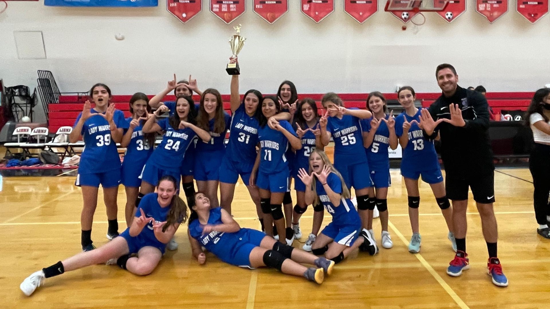 A volleyball team poses for a picture with a trophy
