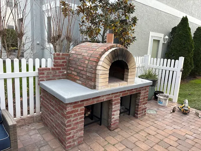 outdoor brick oven with a gray countertop and brick base, on a brick patio built by stone works masonry inc.