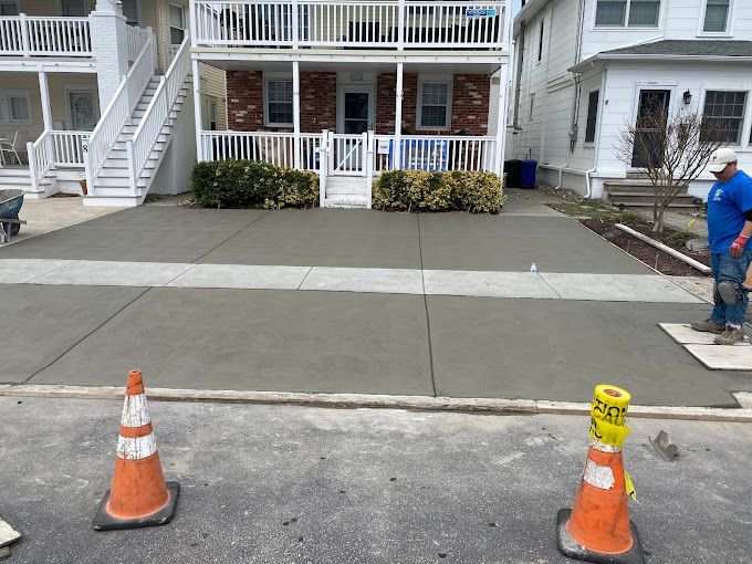 A stone works masonry inc. employee is working on a concrete driveway in front of a house