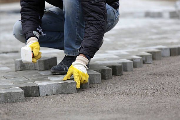 A man wearing yellow gloves is laying bricks on a sidewalk.
