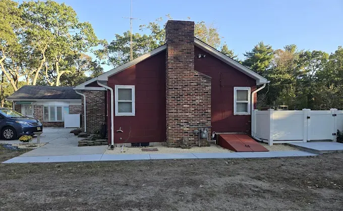 Red-sided house with a brick chimney and white trim, with new concrete walkway and driveway built by stone works masonry inc.