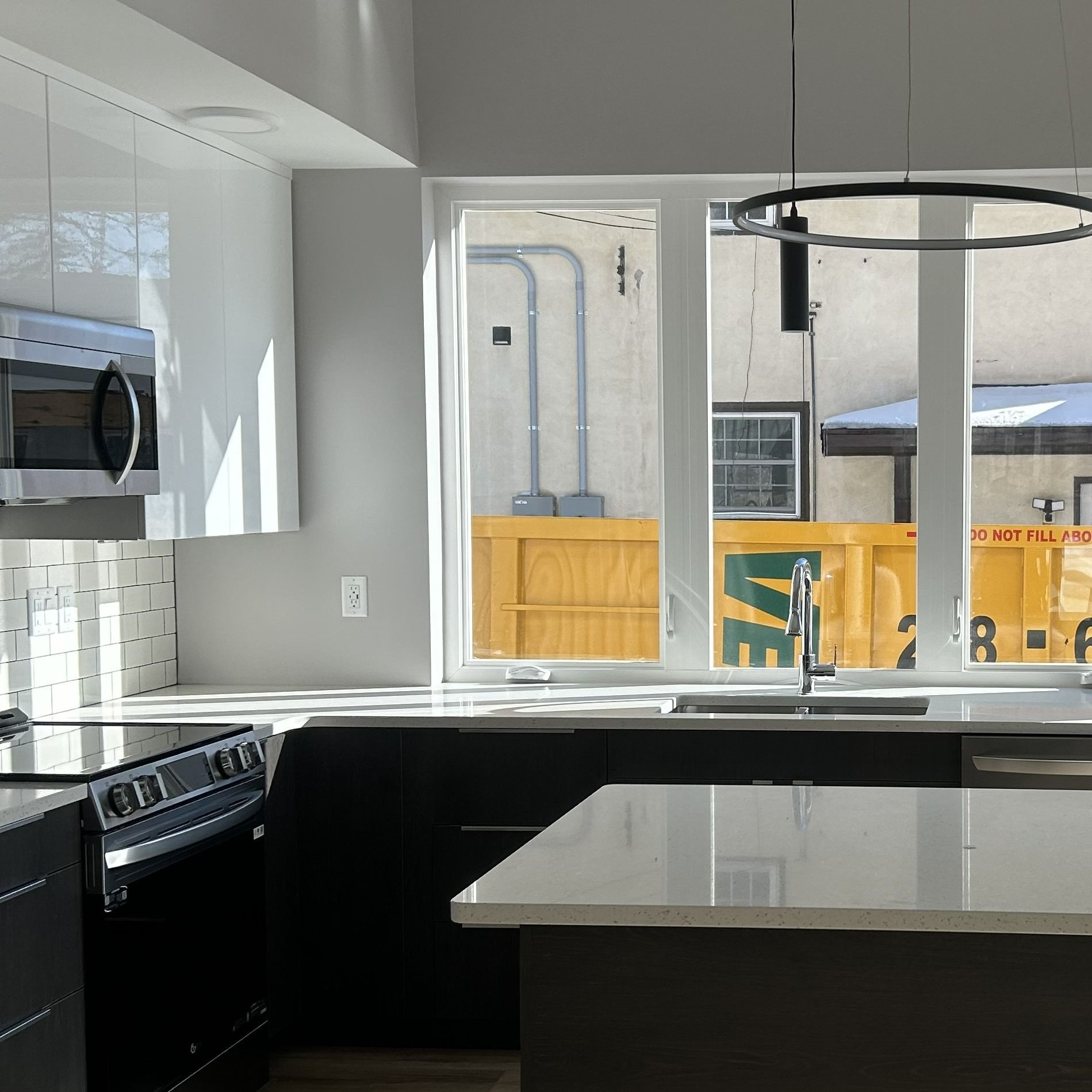 Modern kitchen with black and white cabinets, large window, and overhead light.