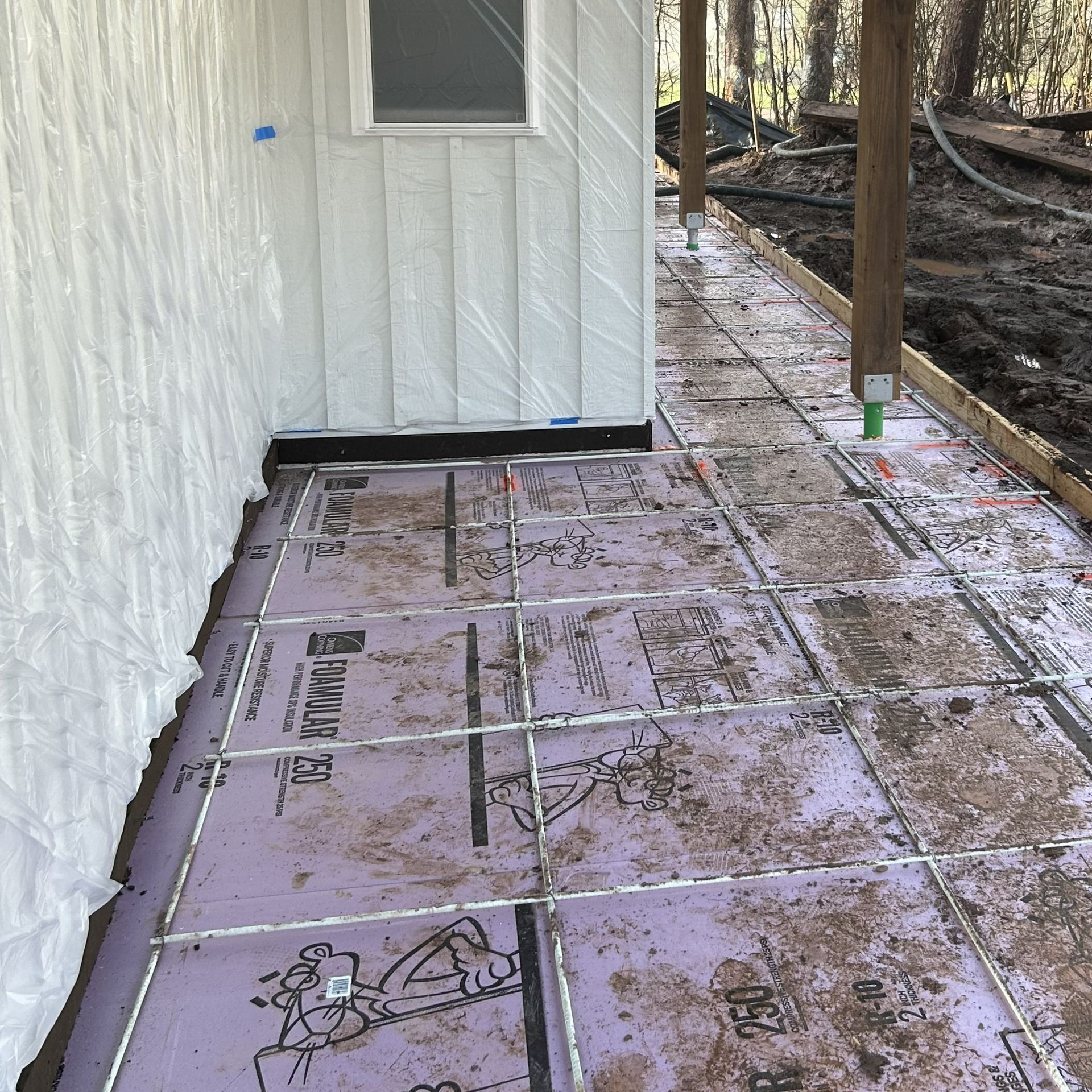 Construction site: pink foam insulation, metal grid, and exterior wall with a small window.