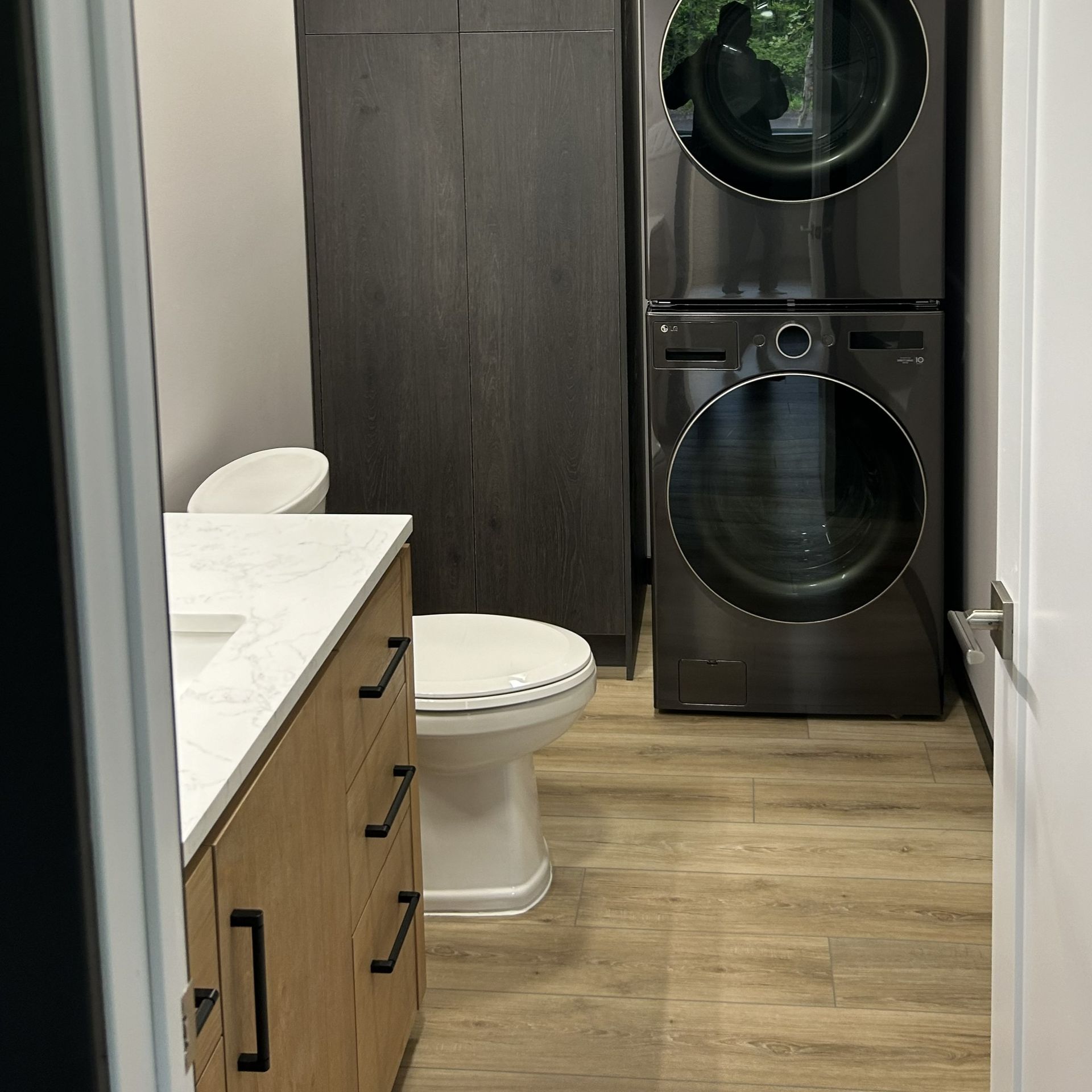 Bathroom with stacked washer and dryer, toilet, wood cabinets, and light wood-look flooring.