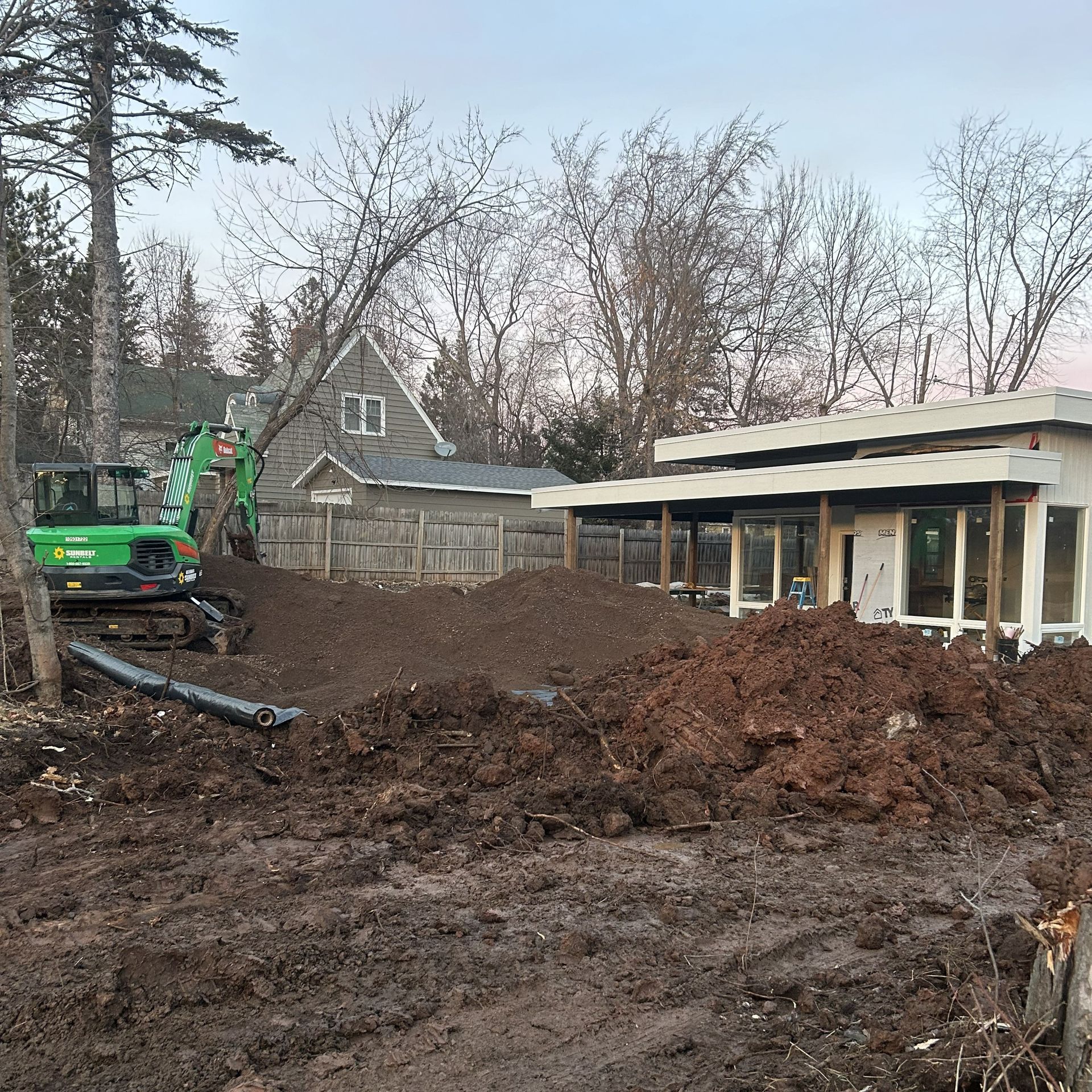 A construction site with a green excavator, dirt piles, and a modern building with large windows.