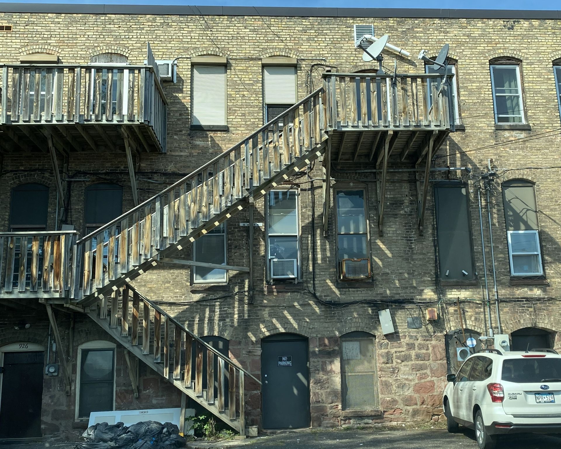 Exterior of brick building with wooden fire escapes and a white SUV.