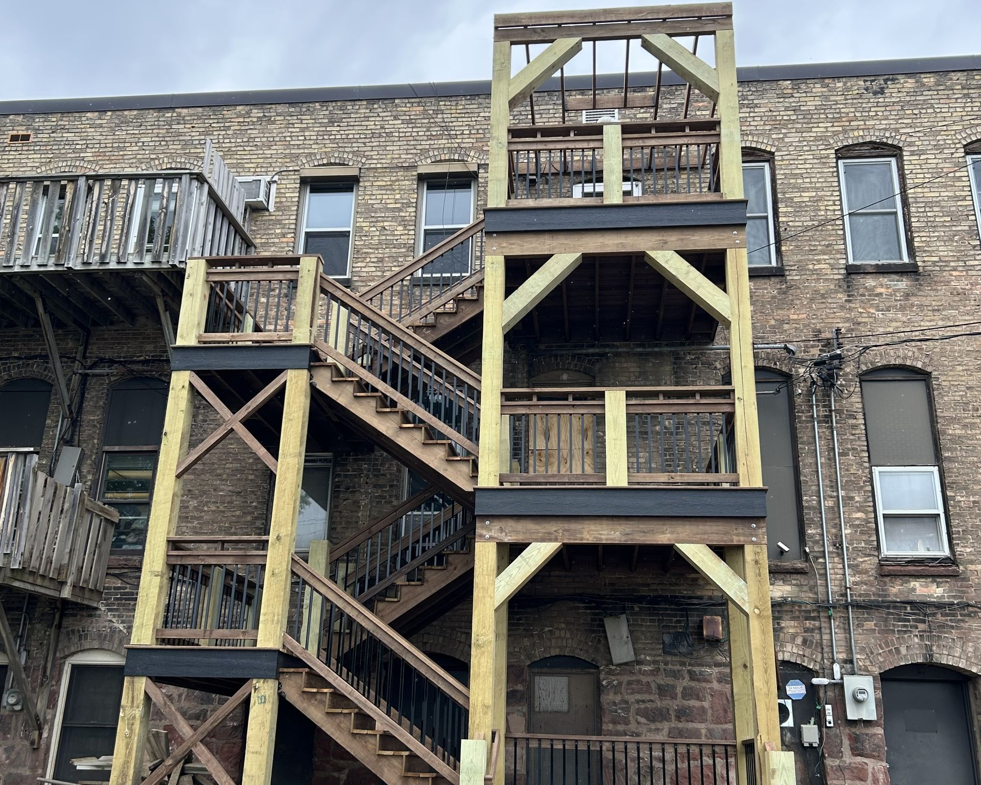 Exterior wooden fire escape stairs against a brick building.