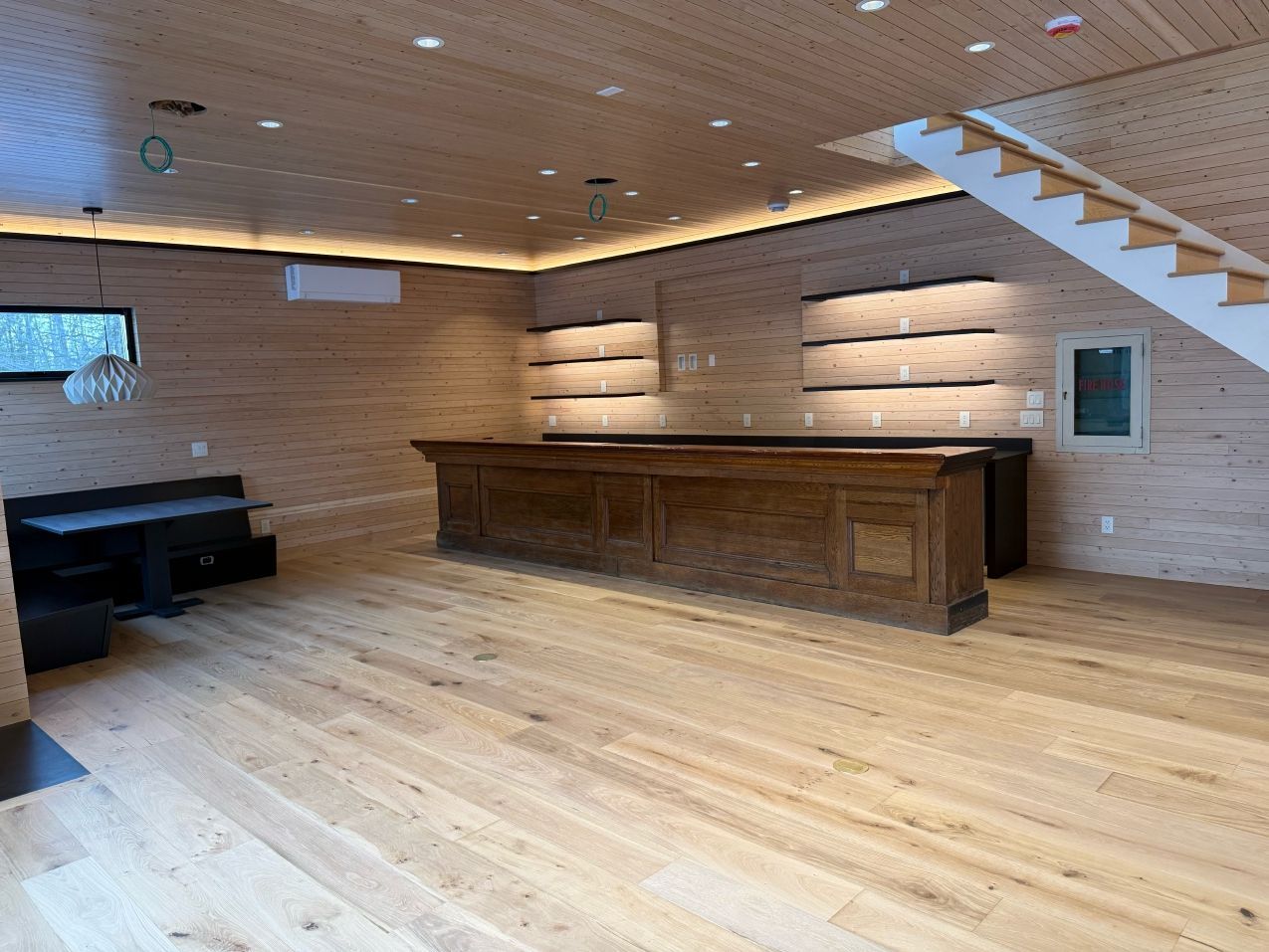 Wooden bar in a finished basement with wood paneling, recessed lighting, and a staircase.