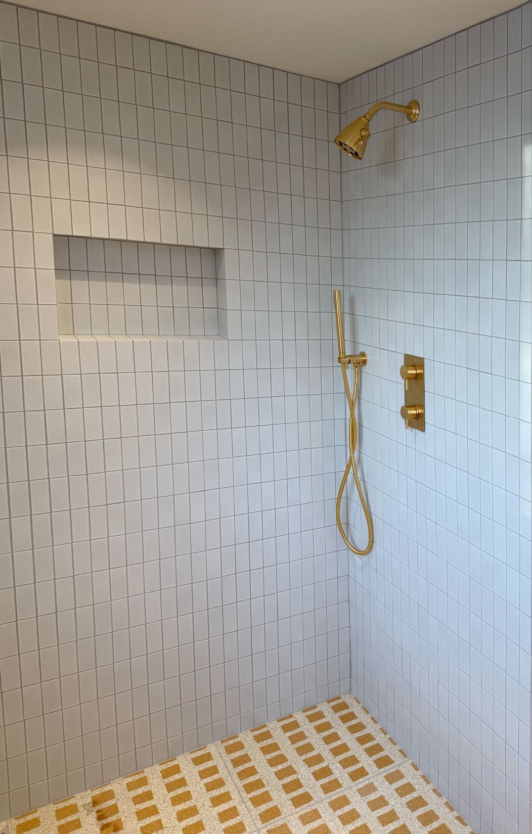 Shower with gold fixtures and textured, light blue tiled walls and floor.