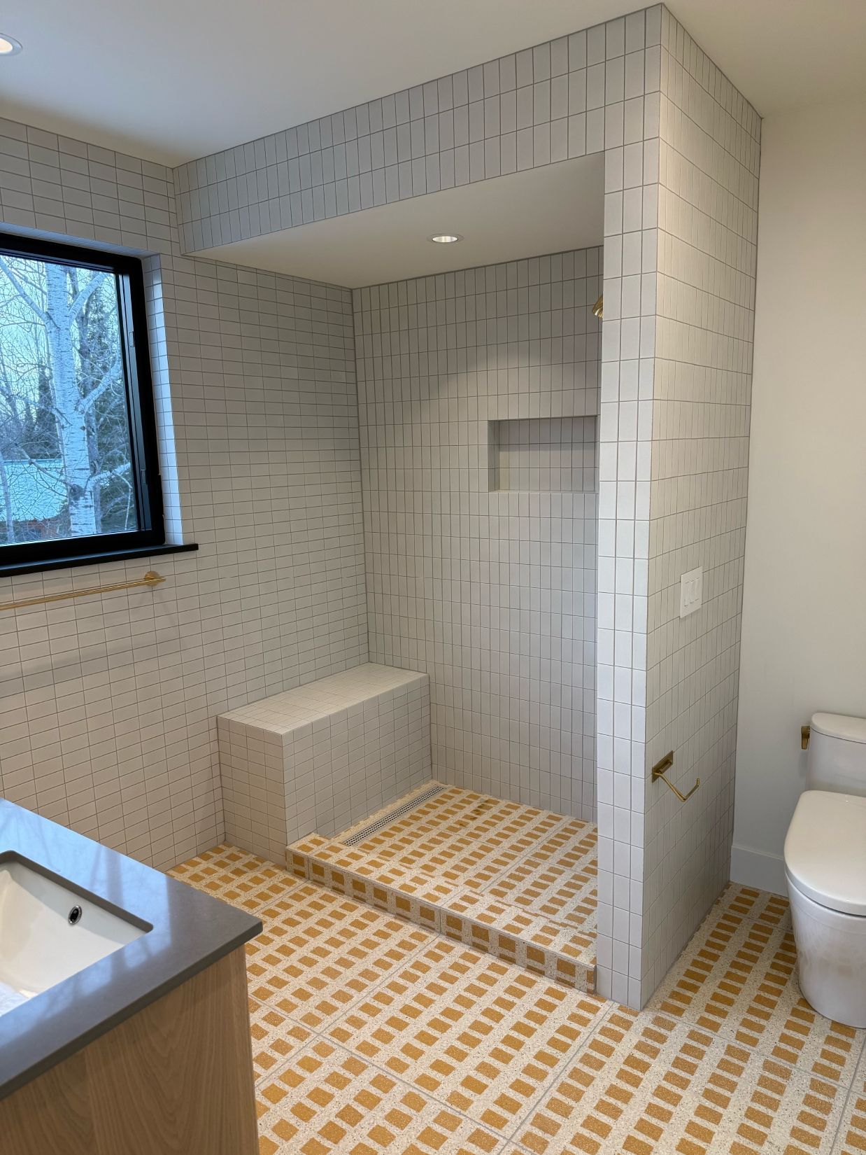 Newly tiled bathroom with yellow and white patterned floor, white tiled shower, toilet.