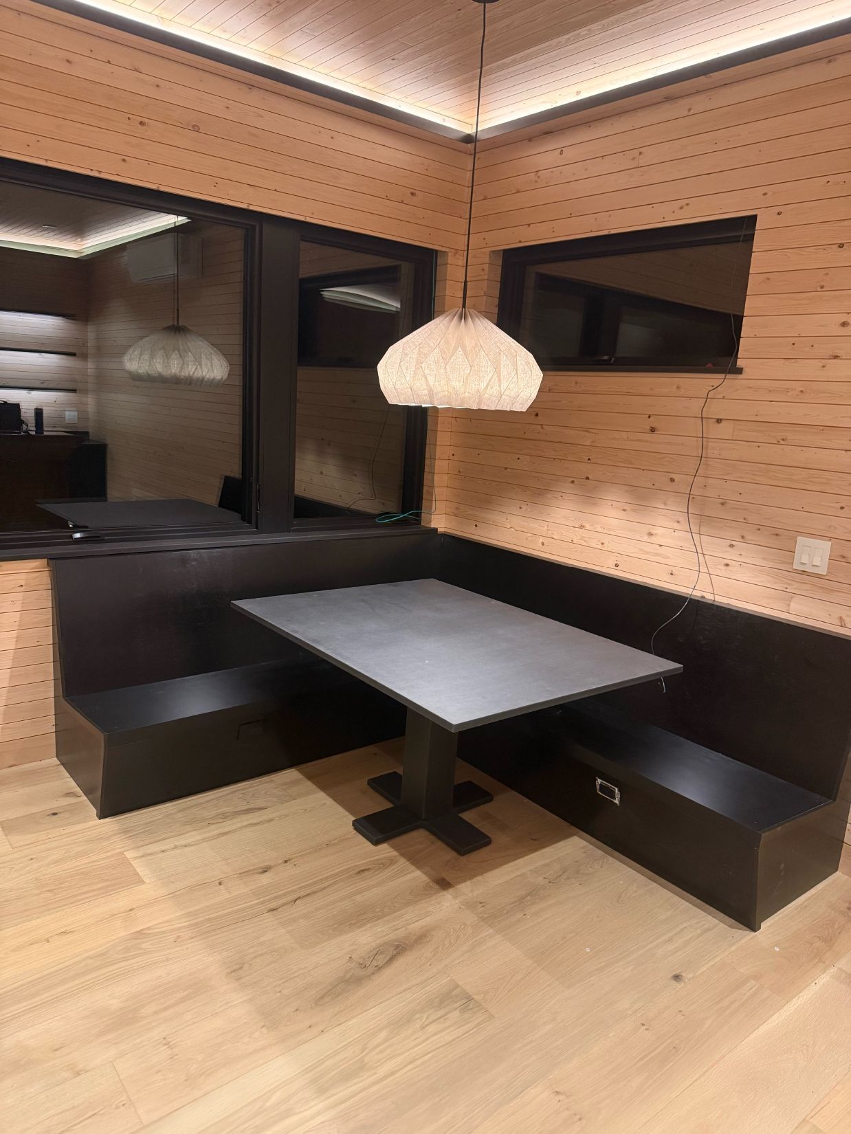 Restaurant booth with dark seating and a gray table. A woven pendant light hangs above.