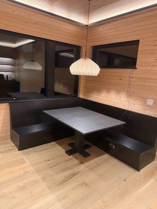 Corner booth seating in a room with wood paneling and a hanging woven light fixture over a dark table.
