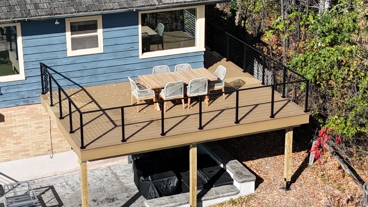 Wooden deck with black railing, table, and chairs outside a blue house.
