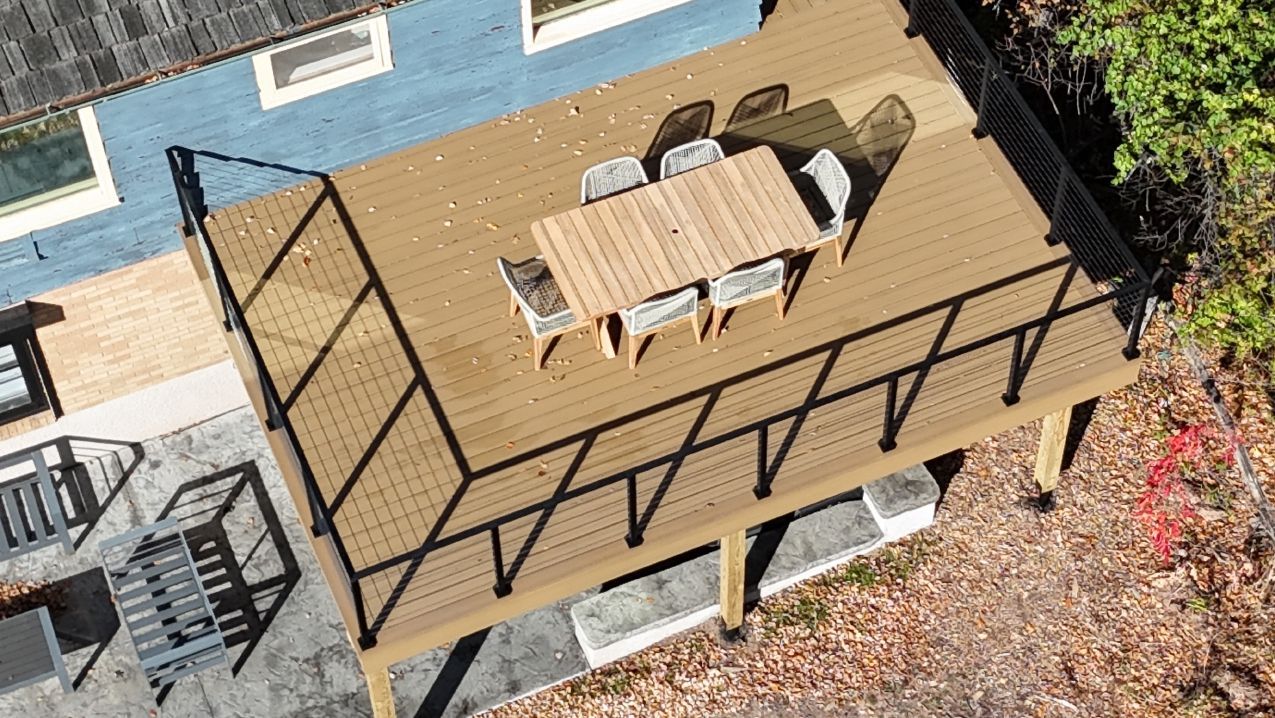 Brown elevated wooden deck with black railings and a table set.