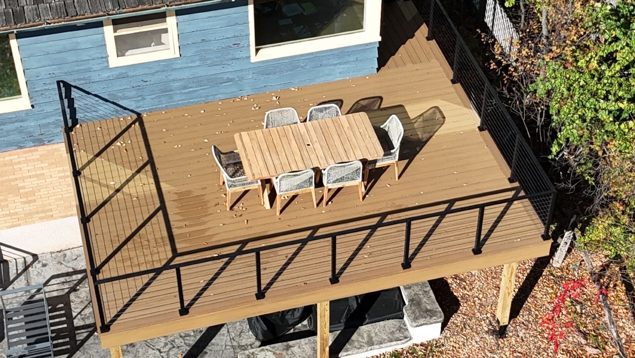 Wooden deck with outdoor dining table and chairs, black railing, attached to a blue house.