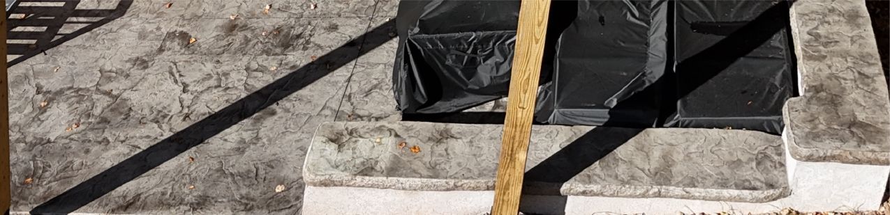 Concrete steps with black plastic and a vertical brown rope. A dark shadow cuts diagonally across.