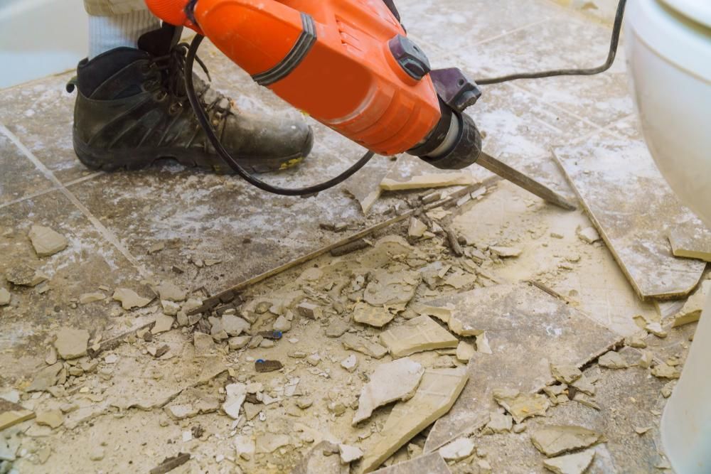 Person Using an Orange Power Tool to Break Up Tile Flooring — ABV Plumbing In Woy Woy, NSW