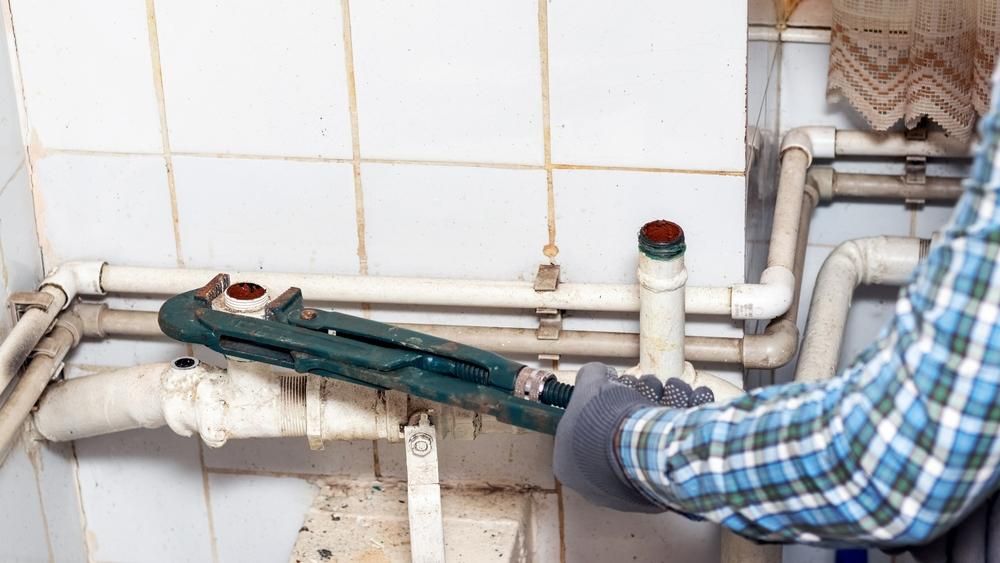 Plumber Using a Large Wrench on Pipes in a Tiled Utility Room — ABV Plumbing In Woy Woy, NSW