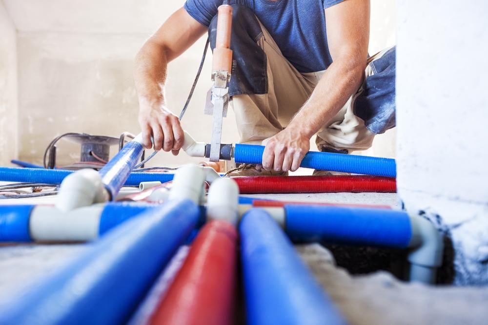Plumber Connecting Blue and Red Water Pipes in a Construction Setting — ABV Plumbing In Tuggerah, NSW